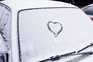 Heart drawn on a car windshield covered with fresh Christmas snow