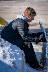 Fototapeta na wymiar A tired teen boy sits on a snow bank holding a snowboard sled.