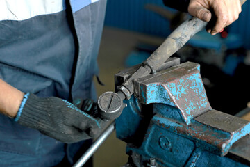A car mechanic repairs a part of the car. An employee of an auto repair shop has clamped the steering rod in a vise and is repairing it. Close-up