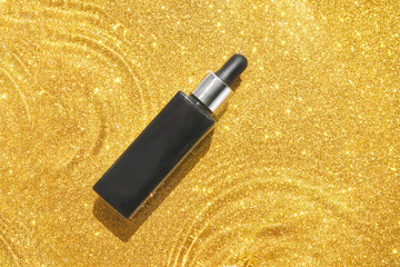 Water circle with gold sparkles background. Yellow glitter backdrop. Golden texture. Black serum bottle. Copyspace mockup. Dreamy shiny design detail. Medical drop
