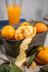 Several ripe tangerines with leaves in a container lie on a white table against a light background. Rustic style copyspace.