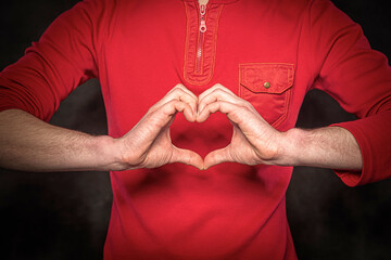 A man shows a heart symbol on a dark background.