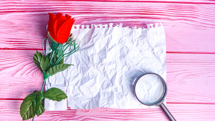 Crumpled blank paper, red rose and magnifying glass on wooden table, vintage paper top view. love or Valentines day concept.