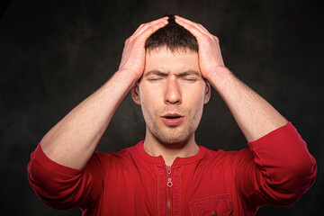 A man holds his head with his hand on a dark background. Headache, migraine, stress.