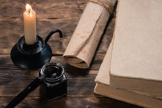 Ball pen, inkwell, parchment scroll, books and burning candle on the table close up.