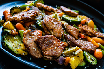 Fried pork steaks and mic of vegetables served on black wooden table
