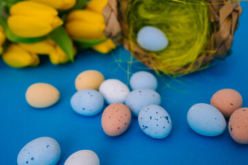 Happy Easter. Easter holiday decorations on trendy colored classic blue background. Creative spring composition with Easter elements - flowers and eggs in basket. Celebrating Easter concept at spring.