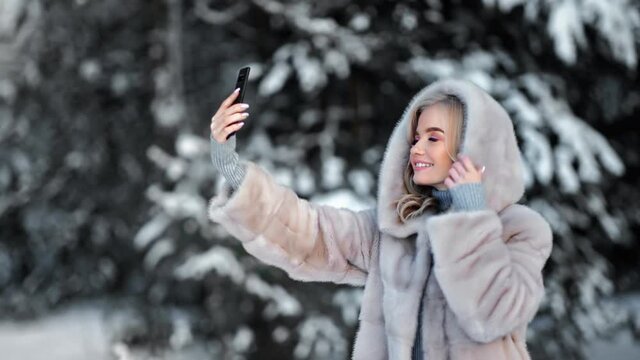 Woman in fur coat taking selfie at winter forest use smartphone. Shot on RED Raven 4k Cinema Camera