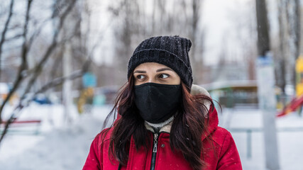 Fototapeta na wymiar A woman in a medical mask in winter clothes stands on the street in winter. Concept: protection against coronavirus