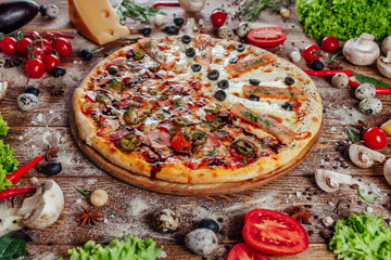 The pizza is surrounded by raw ingredients on the boards