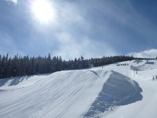 View of a large man-made jump in a ski resort terrain park on a sunny winter day