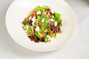 Vegetable vegetarian salad with tomatoes, peppers and onions on white table.