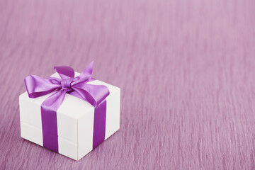 Gift box with purple bow on pink background, shallow depth of sharpness