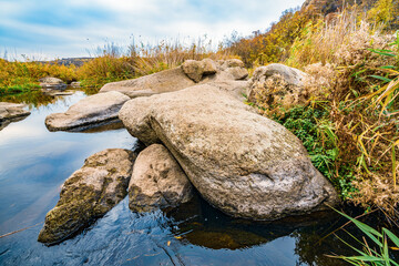 A fast clean stream runs among smooth wet stones surrounded by tall dry lumps