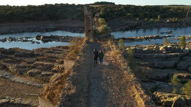 Caucasian couple drone aerial view walking on abandoned destroyed Ajuda bridge crossing Guadiana river between Portugal and Spain, at sunrise