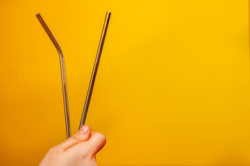 A metal cocktail tube is held by a female hand on a yellow background with a place for text.
