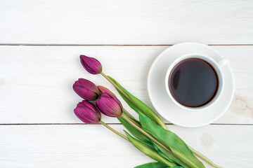 March 8, tulips and coffee in a white cup on a light wooden background. Top view, with space to copy. Concept of festive backgrounds, spring.