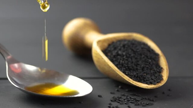Glass bottle of black cumin seed essential oil , Nigella Sativa in scoop on black wooden background, oil dripping