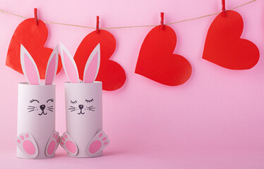 Cute paper bunnies with red hearts on pink background
