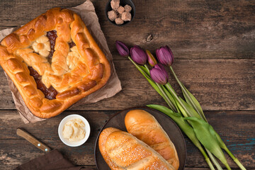 Fruit cake, buns and a bouquet of tulips on a wooden background. Top view with space to copy. The concept of culinary backgrounds, the 8th of March.
