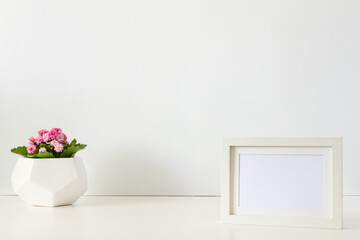 A desk against a white wall. Copy space. Pink flower in a geometric pot. White mockup frame.