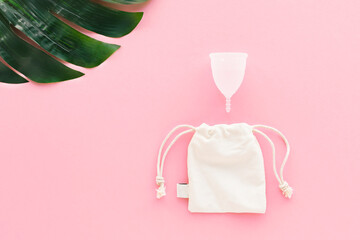 White menstrual Cup on pink background with green leaf . Alternative feminine hygiene product during the period. Women health concept