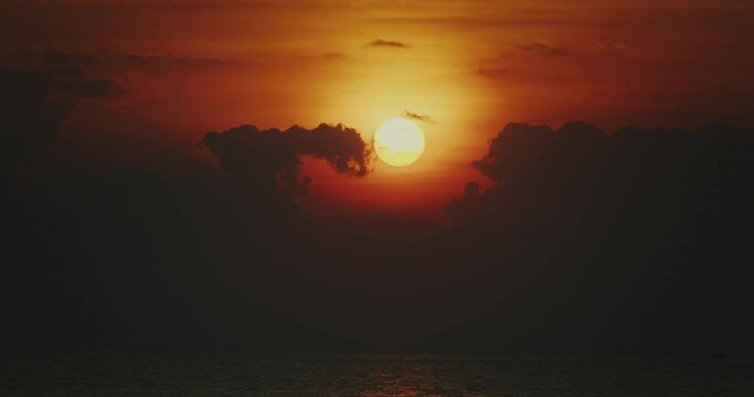 Close up sunset time lapse where sun goes down behind clouds above sea