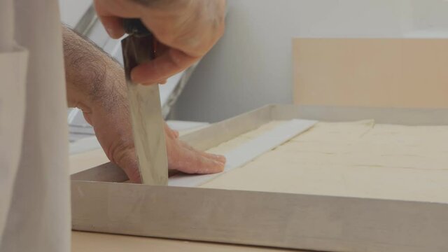 the baker cuts the puff pastry into portions of baklava using a sharp large knife and a white ruler. Cooking Turkish baklava. Close-up. View from the back