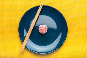 Rice sushi roll with Lava sauce lies on a blue plate with bamboo sticks. Yellow background. Minimalist style. Top view