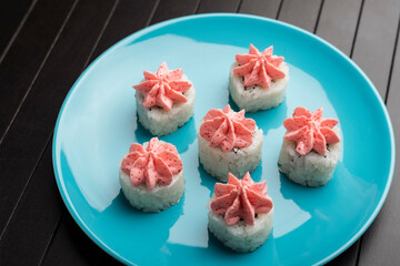 rolls with pink lava sauce on a blue plate, on a wooden table. Serving Japanese food. Close-up