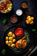 Barbecue chicken drumsticks with baked potatoes on black wooden table