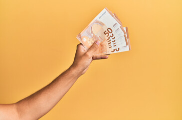Hand of hispanic man holding 50 euro banknotes over isolated yellow background.