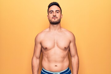 Fototapeta premium Young handsome man with beard wearing sleeveless t-shirt standing over yellow background with serious expression on face. Simple and natural looking at the camera.