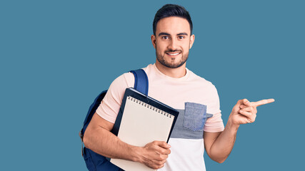 Young handsome man wearing student backpack and notebook smiling happy pointing with hand and finger to the side