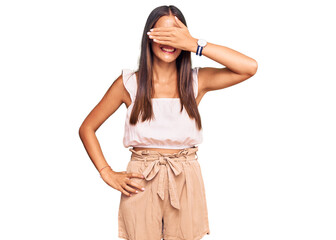 Young hispanic woman wearing casual clothes and glasses smiling and laughing with hand on face covering eyes for surprise. blind concept.