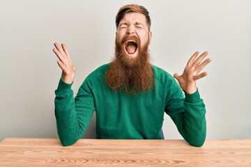 Young irish redhead man wearing casual clothes sitting on the table celebrating mad and crazy for...