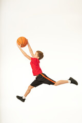 Adorable sporty boy holding basketball ball and jumping