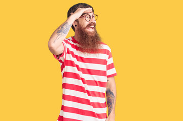 Handsome young red head man with long beard wearing casual clothes very happy and smiling looking far away with hand over head. searching concept.