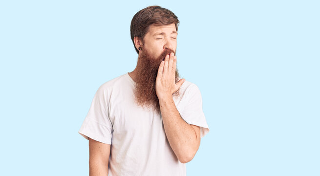 Handsome young red head man with long beard wearing casual white tshirt bored yawning tired covering mouth with hand. restless and sleepiness.