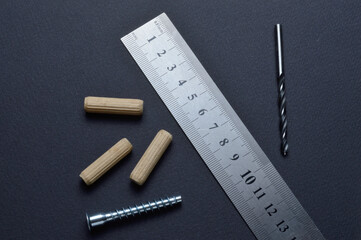 furniture assembly fittings, ruler and drill. lie on a dark background. close-up.