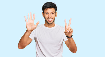 Fototapeta premium Young handsome man wearing casual white tshirt showing and pointing up with fingers number seven while smiling confident and happy.