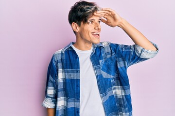 Young hispanic man wearing casual clothes very happy and smiling looking far away with hand over head. searching concept.