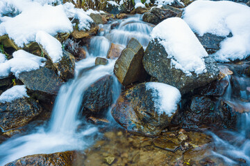 Fototapeta na wymiar Small stream among wet stones and white snow in the picturesque Carpathian mountains in Ukraine