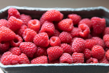 Close-up of a lot of raspberries in a shop filling container in day light. Concept for organic berries, vegetarianism, healthy eating, natural vitamins. Soft selective focus. Horizontal
