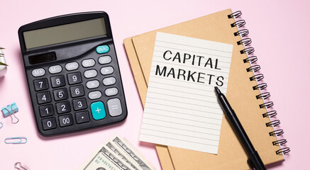 Card with text CAPITAL MARKETS. Keyboard, notebook and pink background