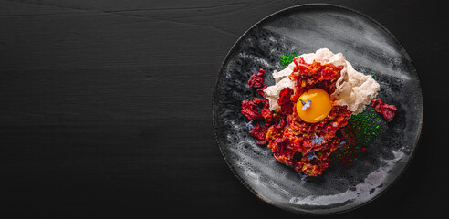 Raw beef meat tartar in plate on black wooden table background