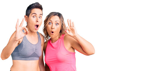 Fototapeta na wymiar Couple of women wearing sportswear looking surprised and shocked doing ok approval symbol with fingers. crazy expression