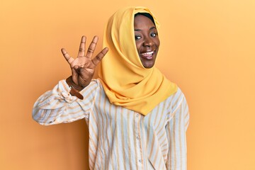 Beautiful african young woman wearing traditional islamic hijab scarf showing and pointing up with fingers number four while smiling confident and happy.