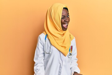 Beautiful african young woman wearing doctor uniform and hijab winking looking at the camera with sexy expression, cheerful and happy face.