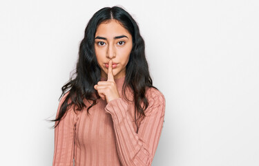 Hispanic teenager girl with dental braces wearing casual clothes asking to be quiet with finger on lips. silence and secret concept.